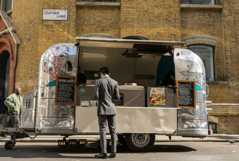A smartly dressed man purchases a Naan wrap from a shiny Revival Trailer street stall seller on Leather Lane in London, UK.
